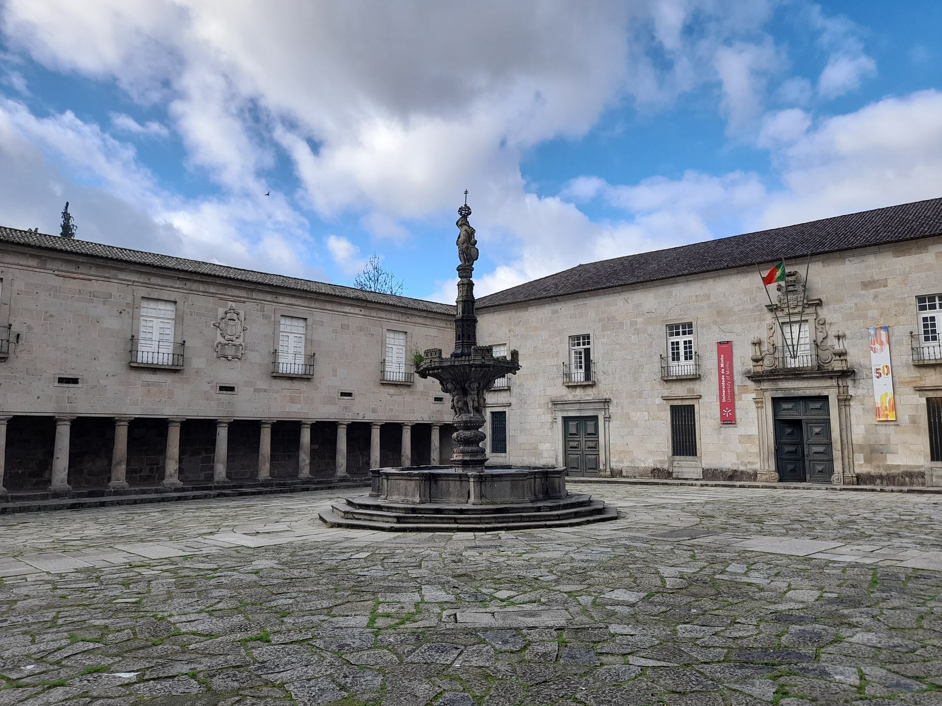 Stone courtyard with a central fountain and historic buildings under a cloudy sky
