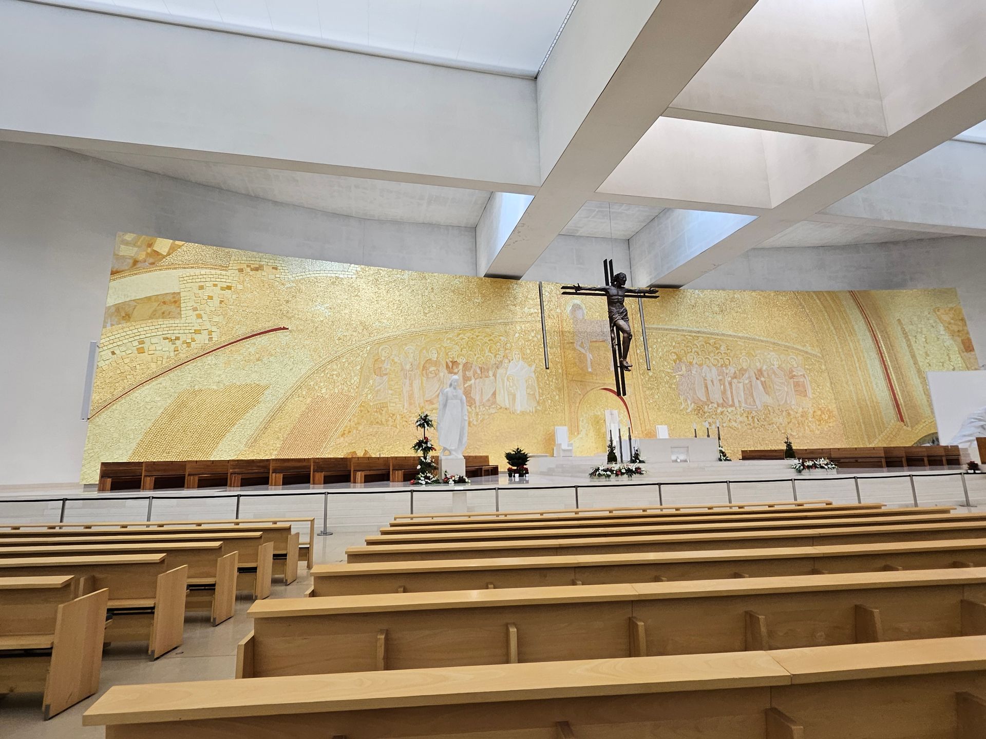 Modern church interior with wooden pews and a gold mosaic altar wall behind a crucifix