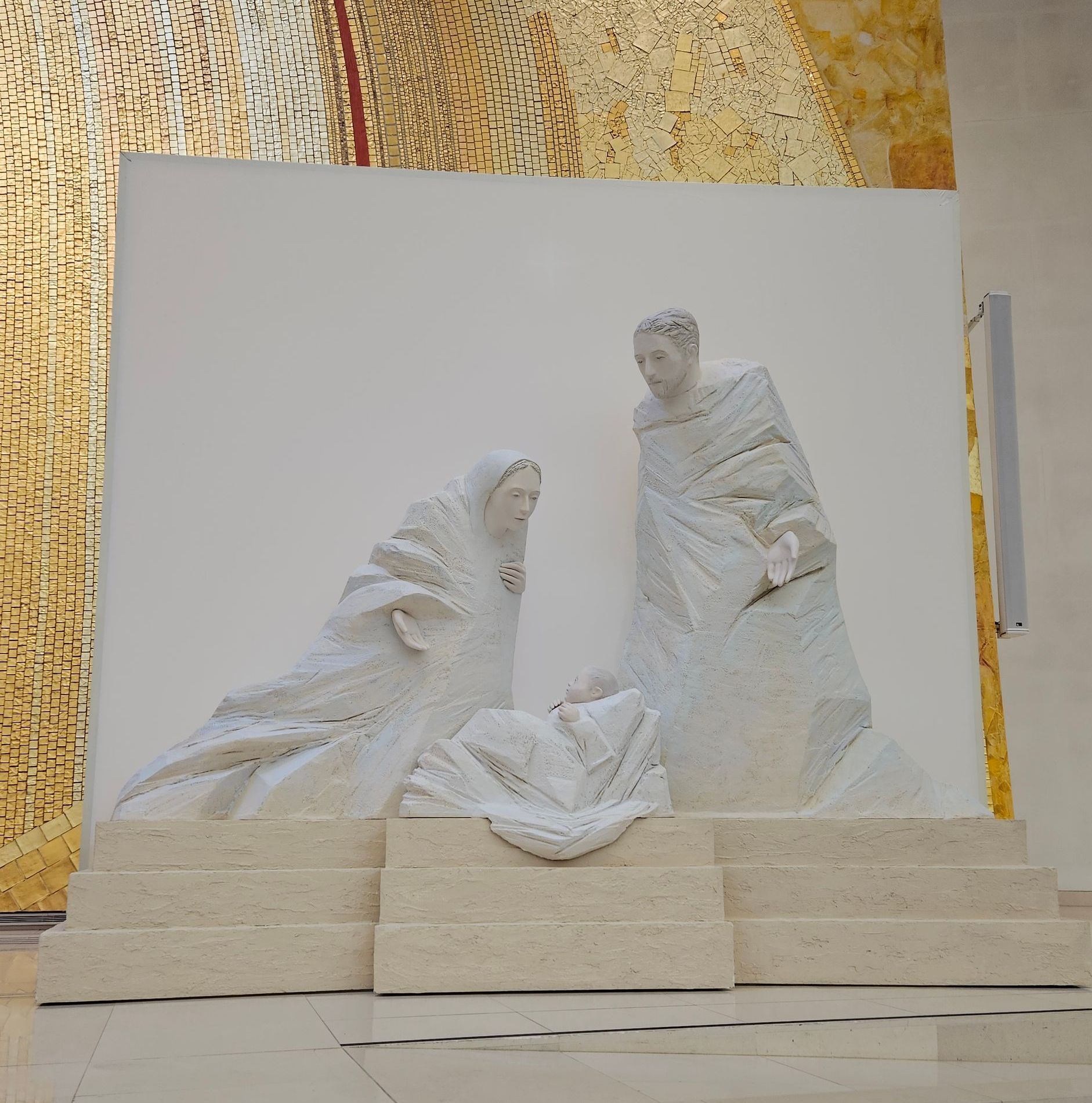White sculpture of two draped figures on a stepped pedestal against a patterned wall