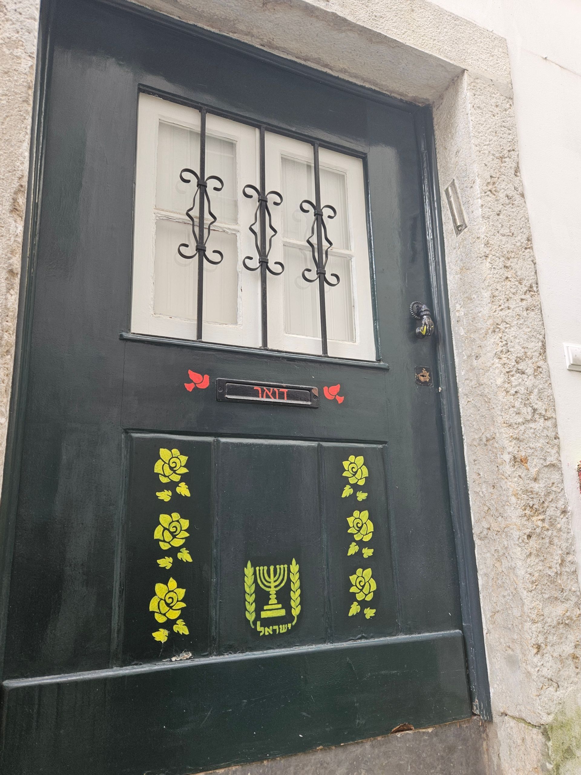 Dark green door with white barred window and yellow floral decorations on a stucco wall