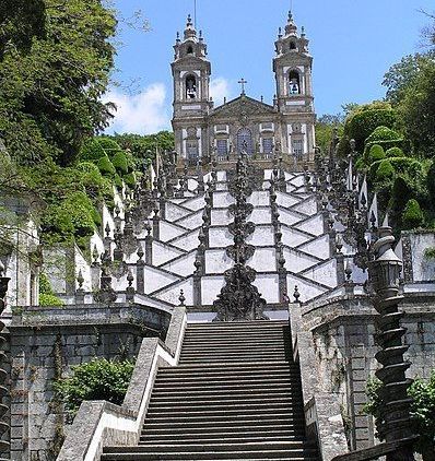 Grand stone staircase leading to a hilltop church with twin towers, surrounded by lush greenery