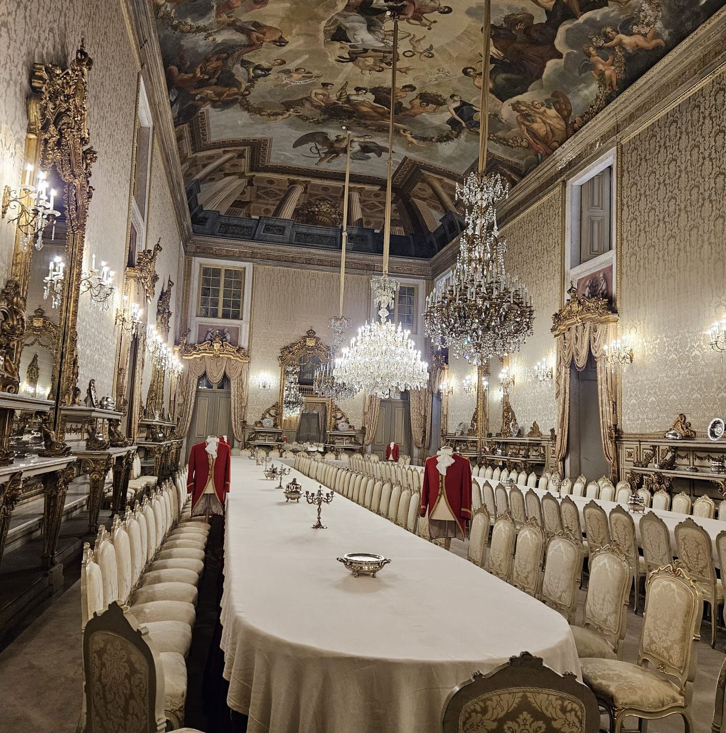 Lavish banquet hall with long white table, ornate chandeliers, and ceiling frescoes