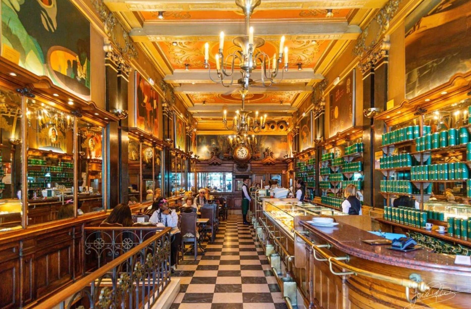 Ornate café interior with gold accents, mirrored walls, chandeliers, and a black-and-white checkered floor