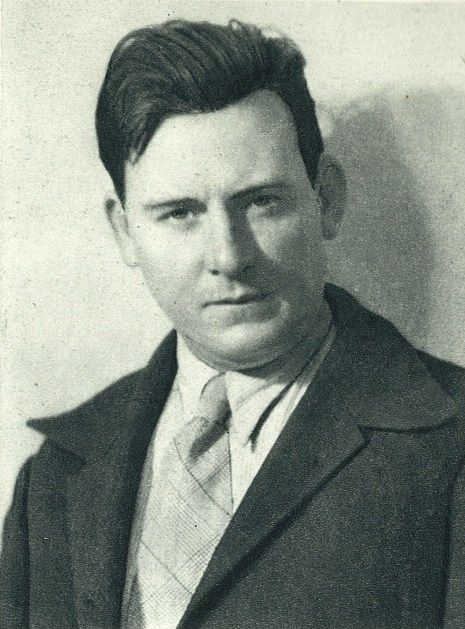 Black-and-white studio portrait of a man in a suit and tie, looking at the camera.