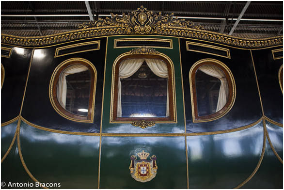 Ornate green and gold royal carriage with windows and crest, shown indoors
