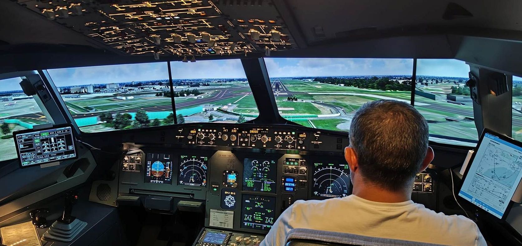 Pilot in a cockpit simulator overlooking a runway and airport at dusk