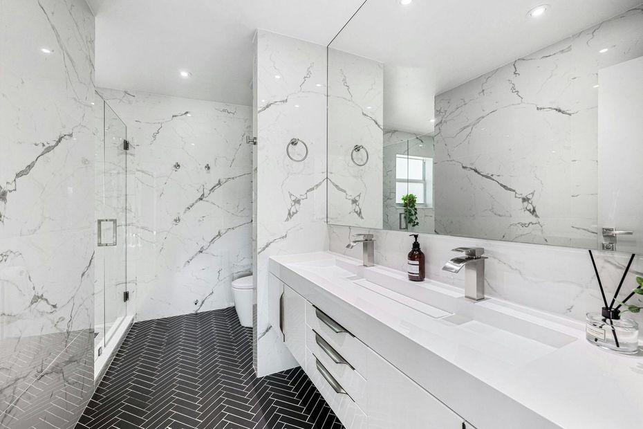 Bright white modern bathroom with marble walls, black tile floor, and long vanity with mirror