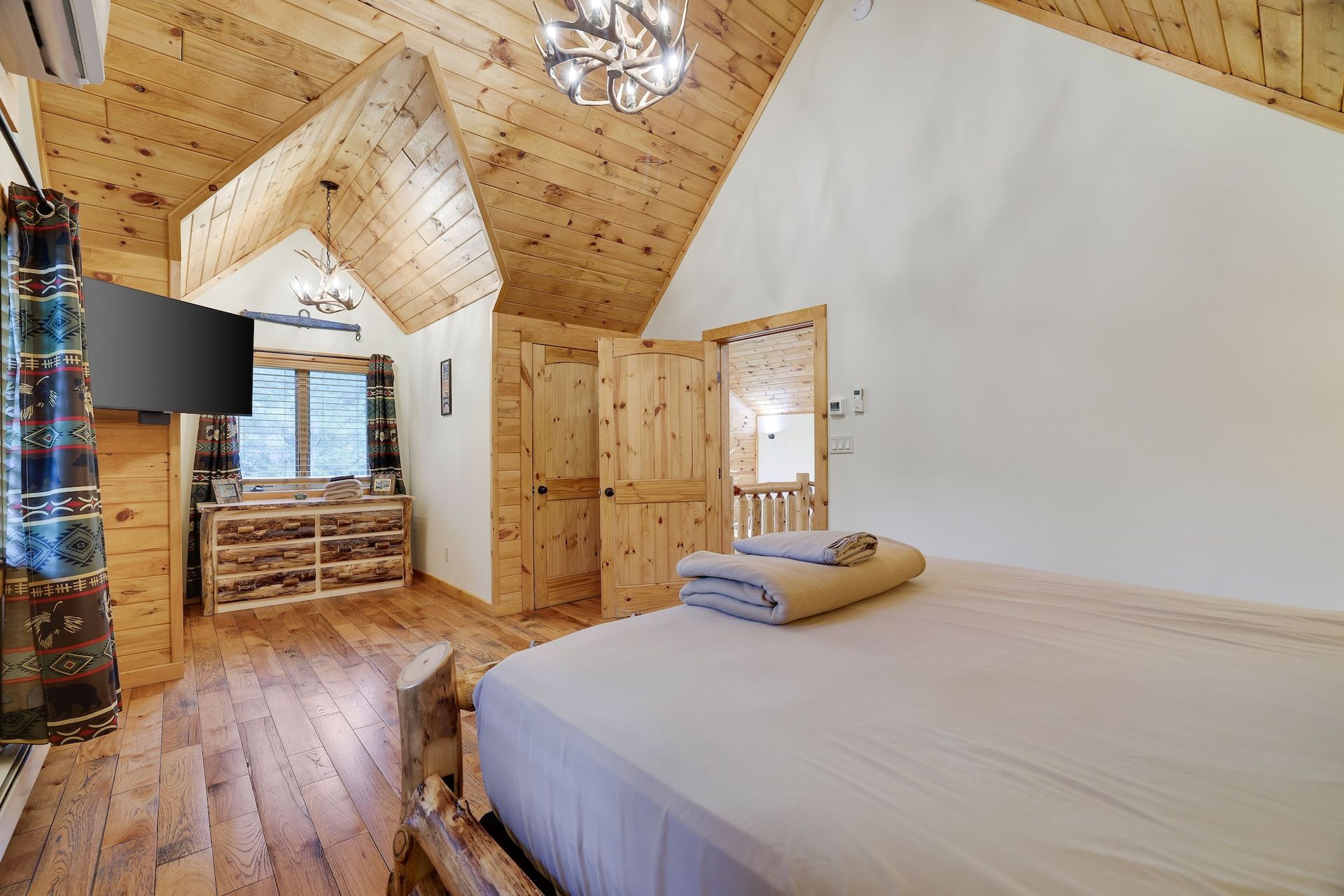 A bedroom with a bed , dresser , television and wooden floors.
