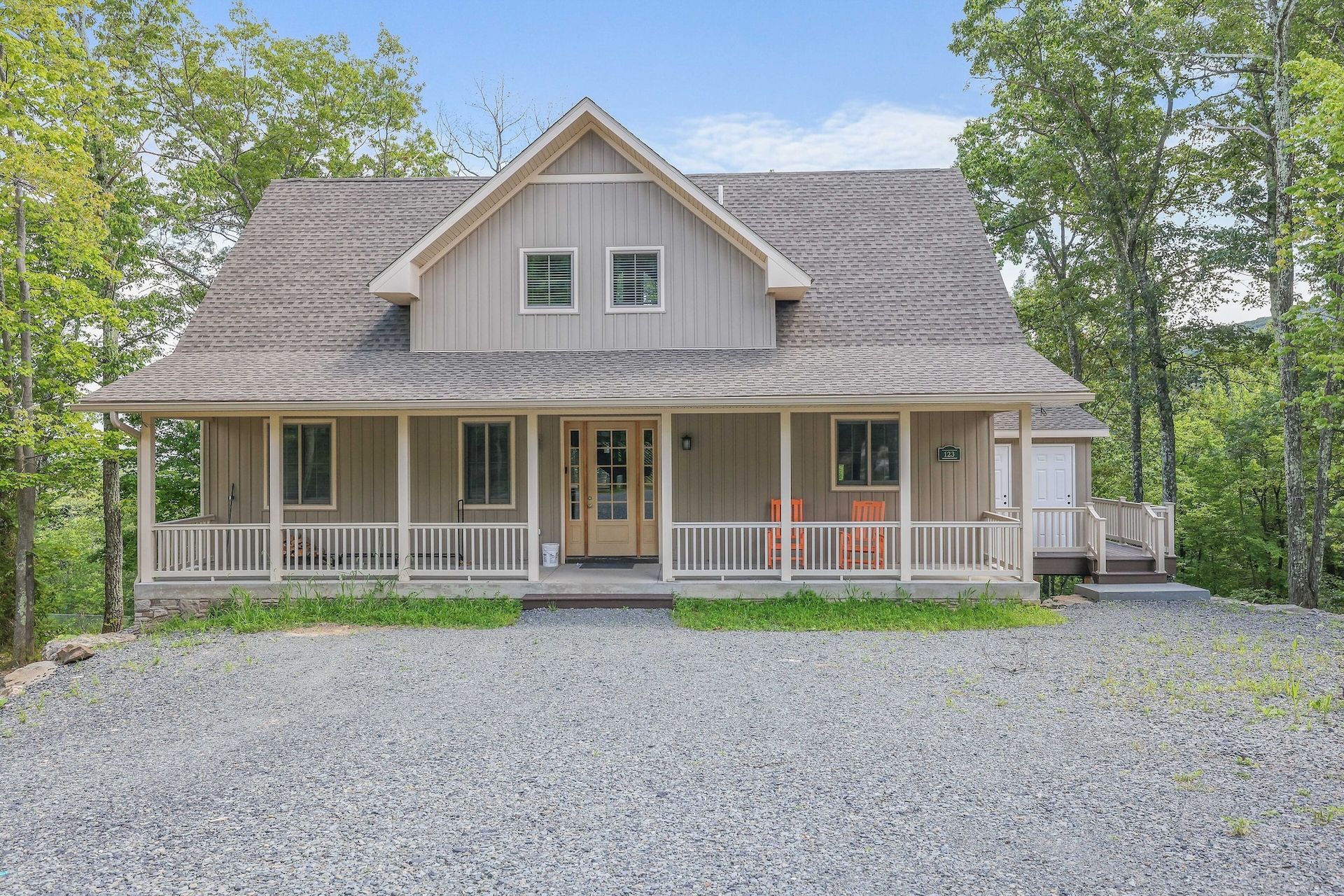 A large house with a large porch is surrounded by trees and gravel.