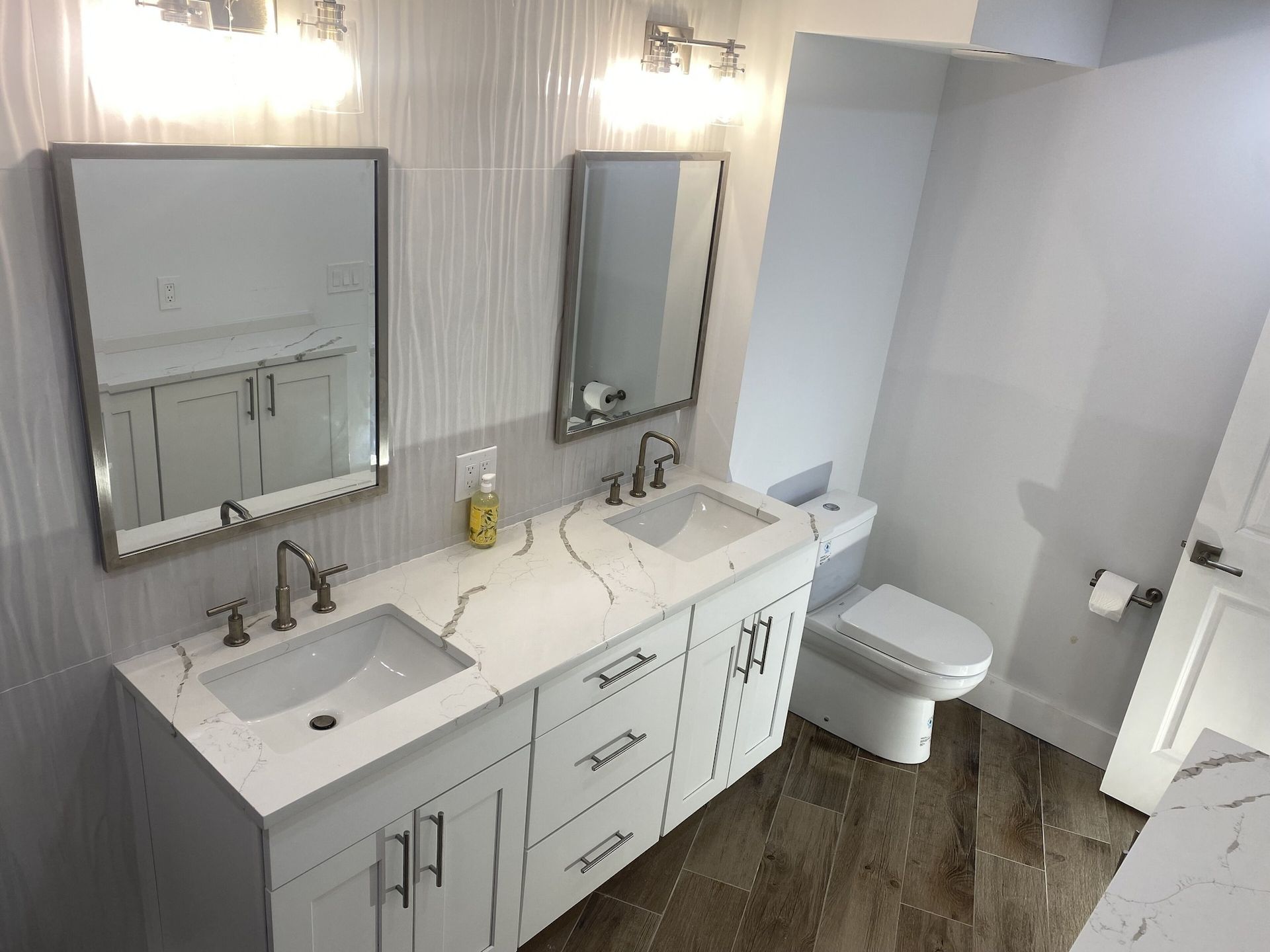 A bathroom with two sinks , a toilet , and two mirrors.