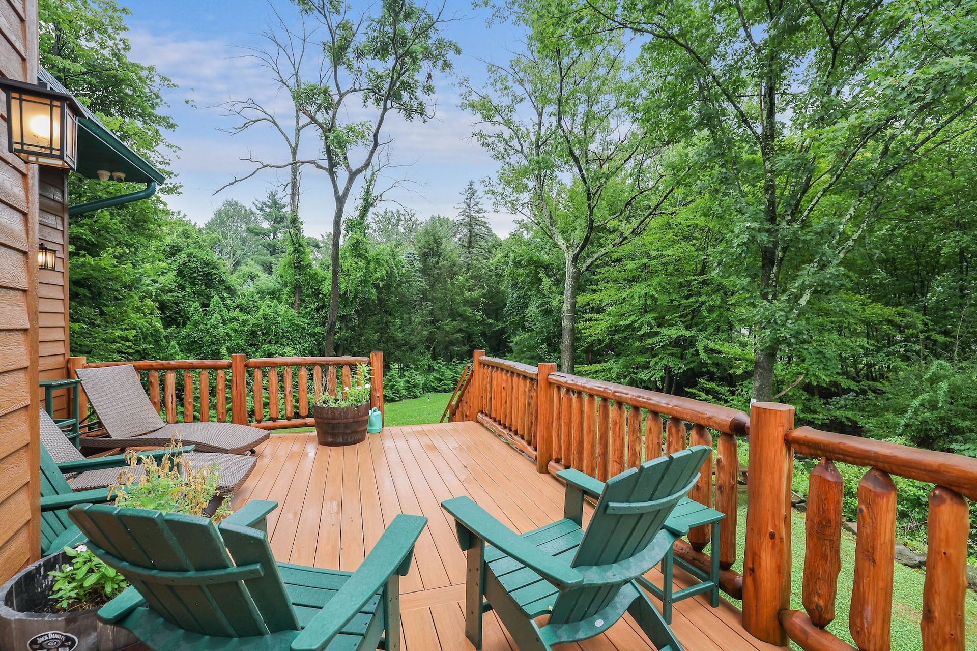 A wooden deck with green chairs and a log railing