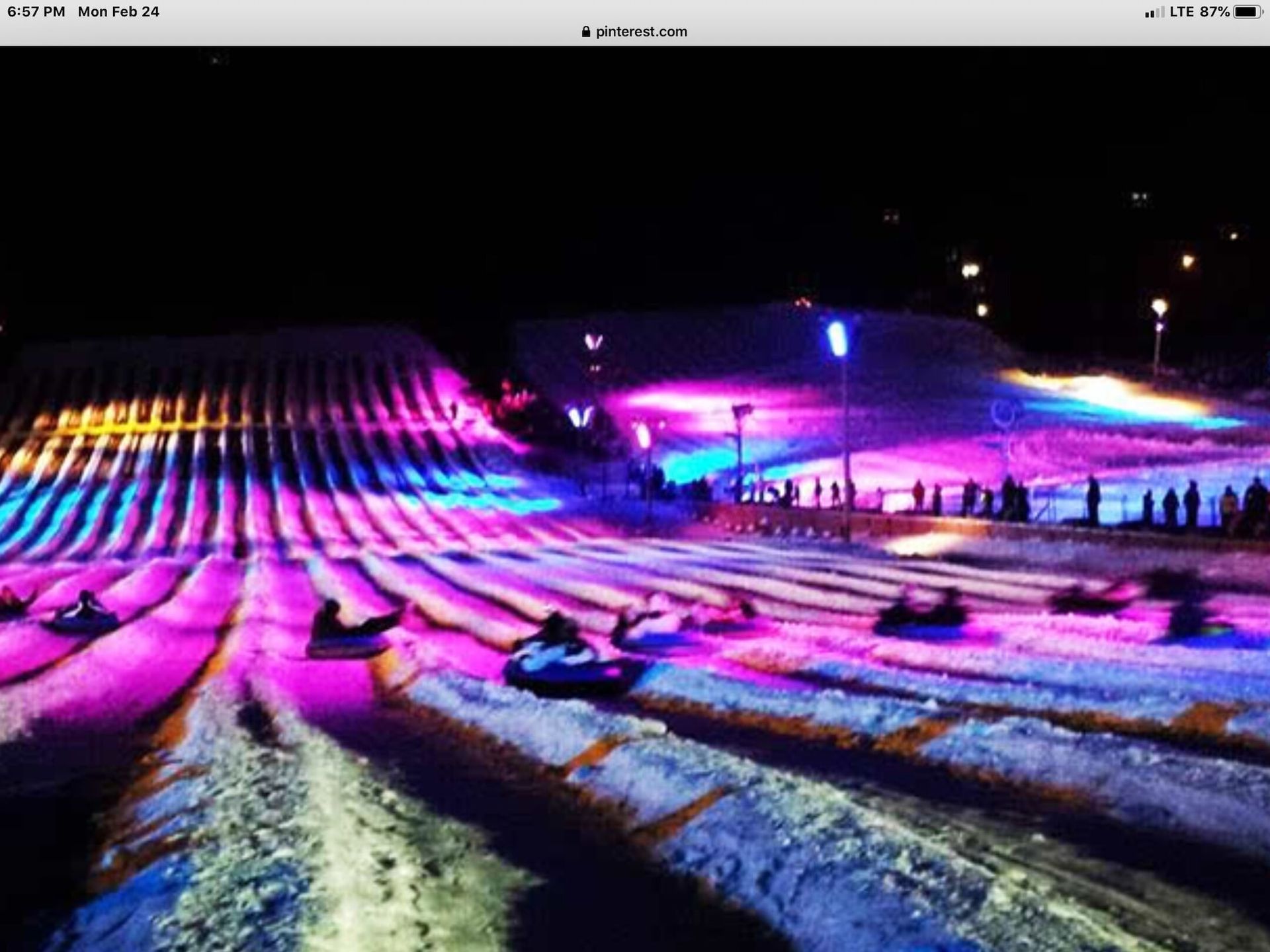 A group of people are sledding down a snow covered hill at night