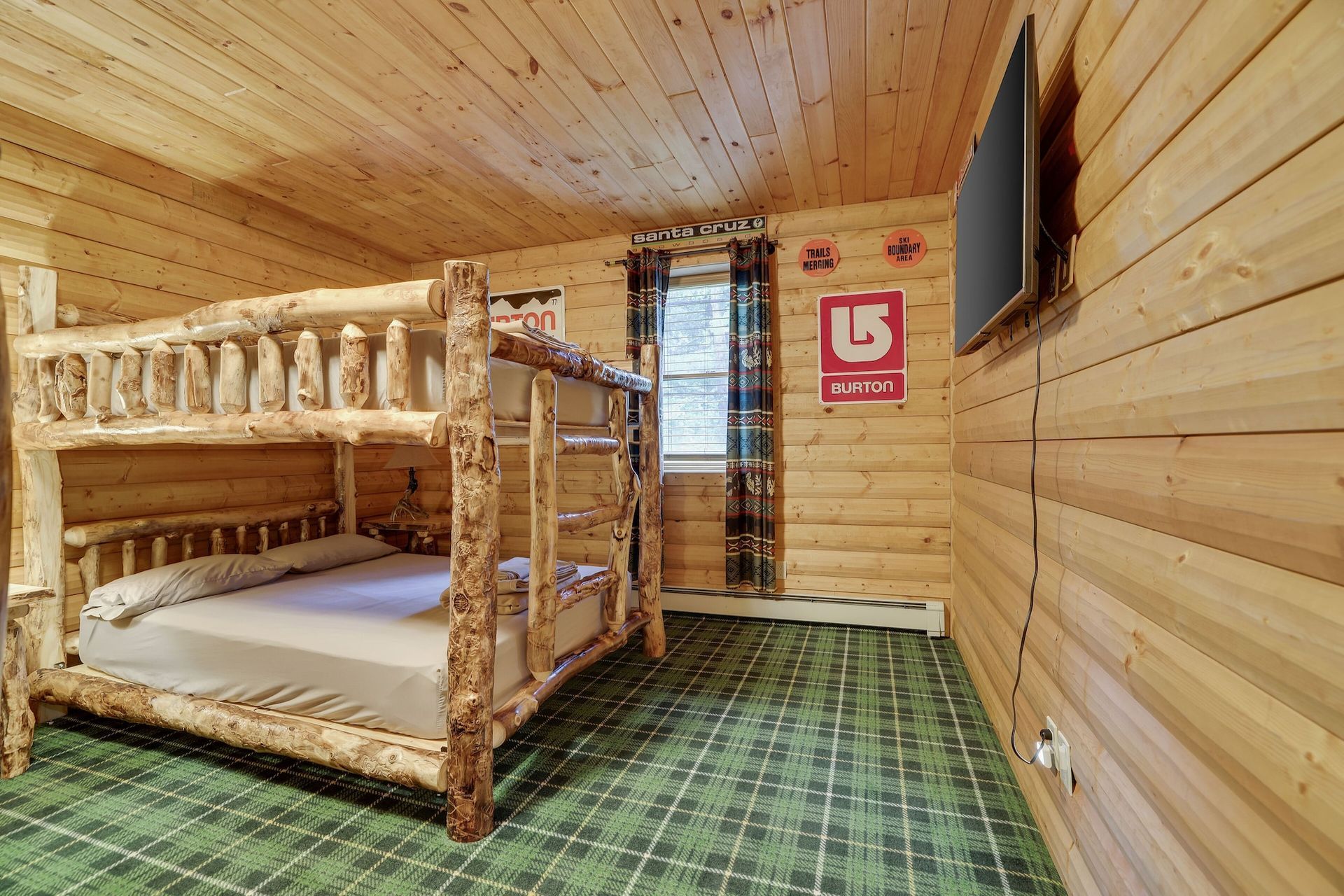 A bedroom in a log cabin with bunk beds and a flat screen tv.