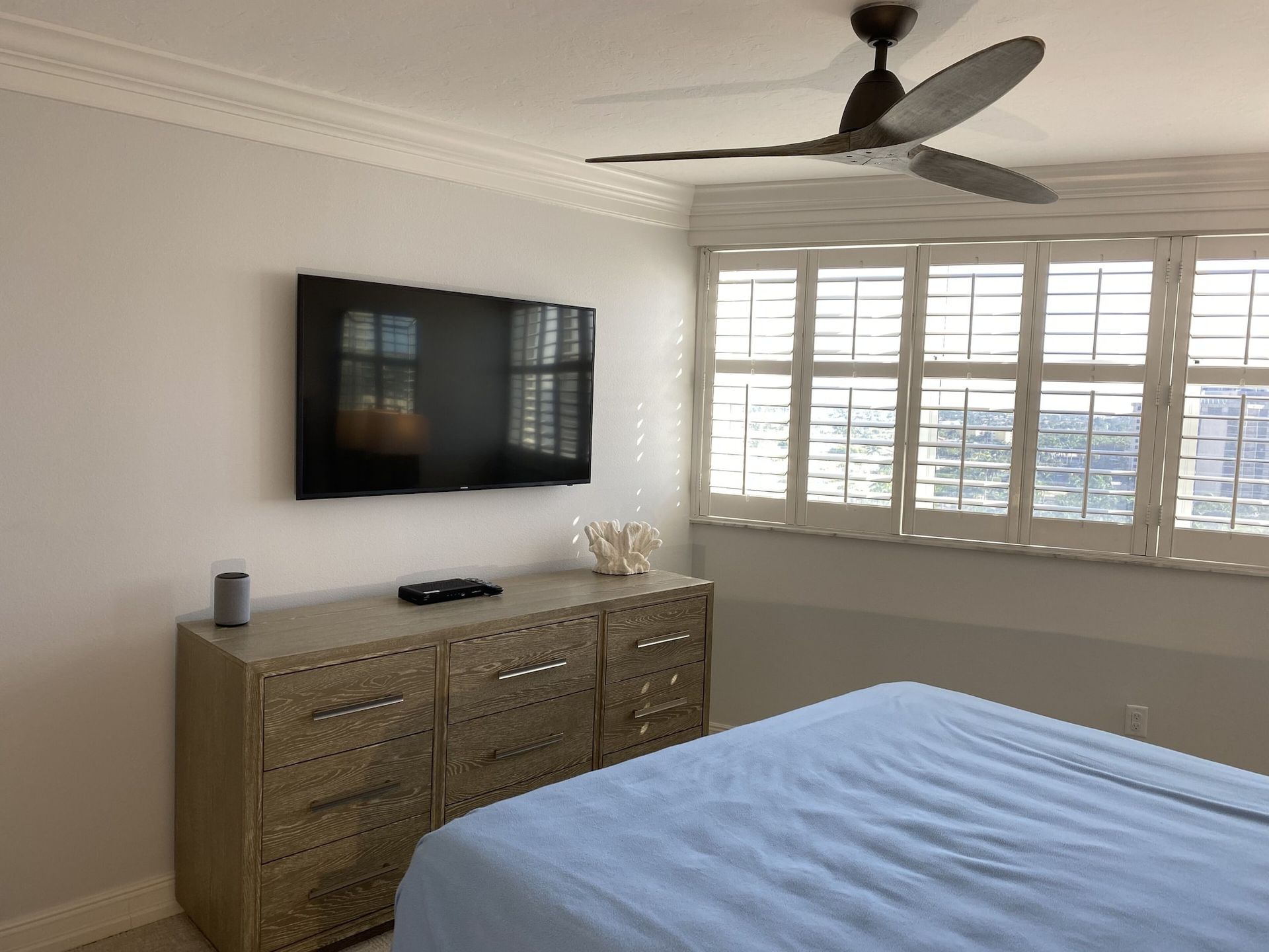A bedroom with a bed , dresser , television and ceiling fan.