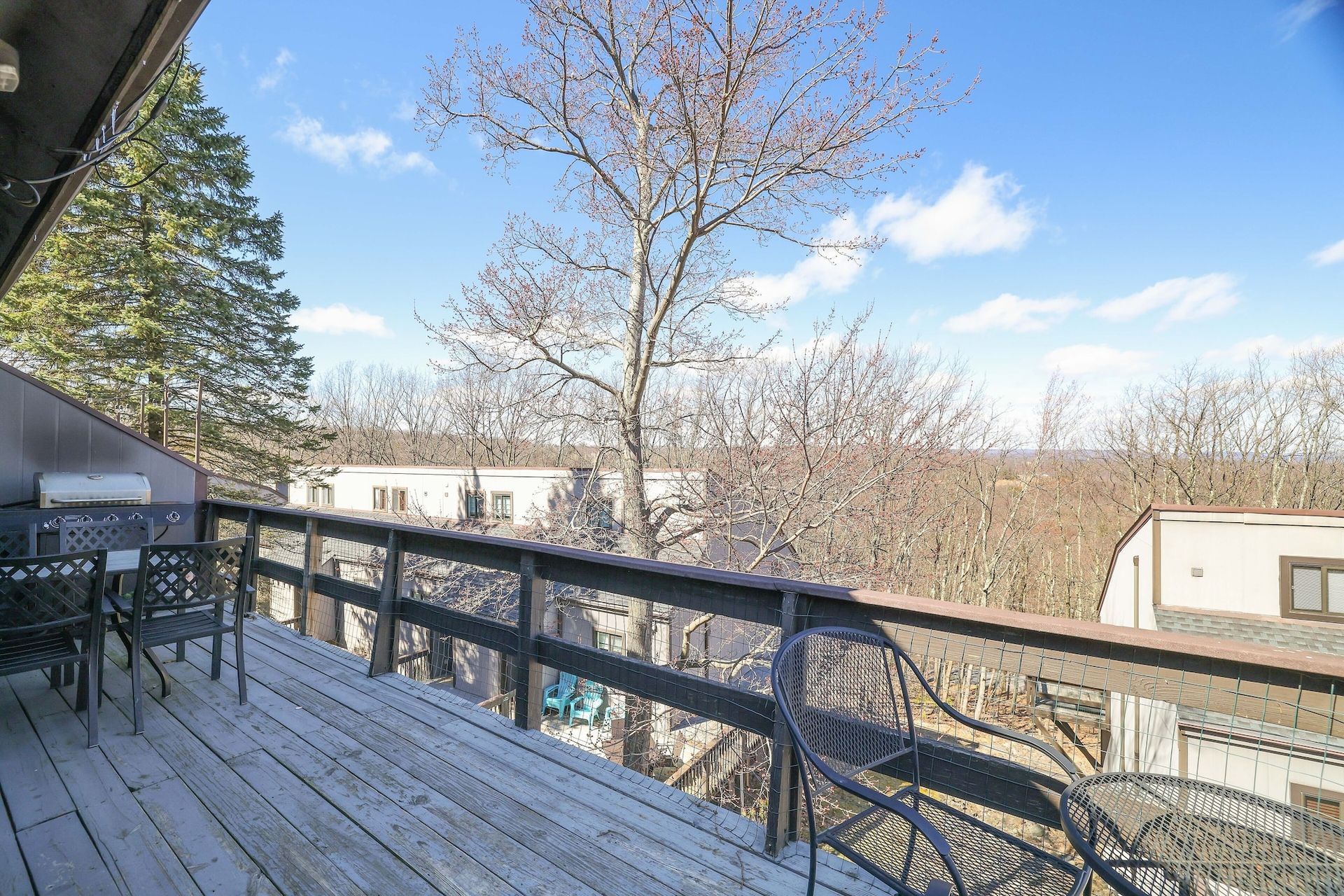 A wooden deck with chairs and a table with a view of a forest.