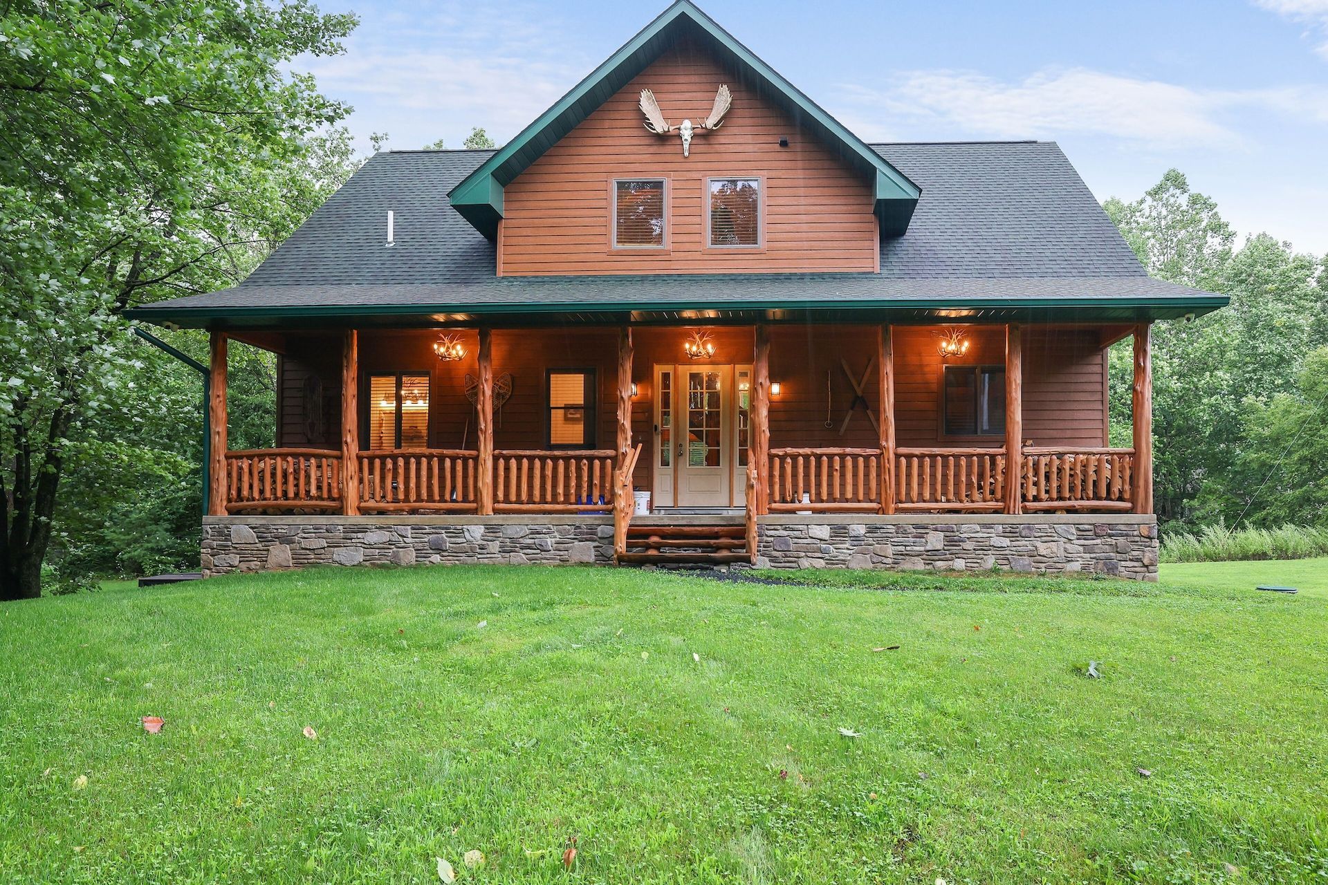 A large log cabin with a large porch in the middle of a lush green field.