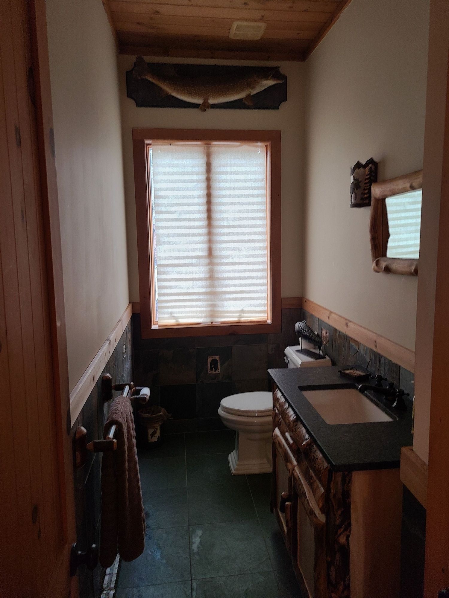 A bathroom with a toilet , sink , mirror and window.