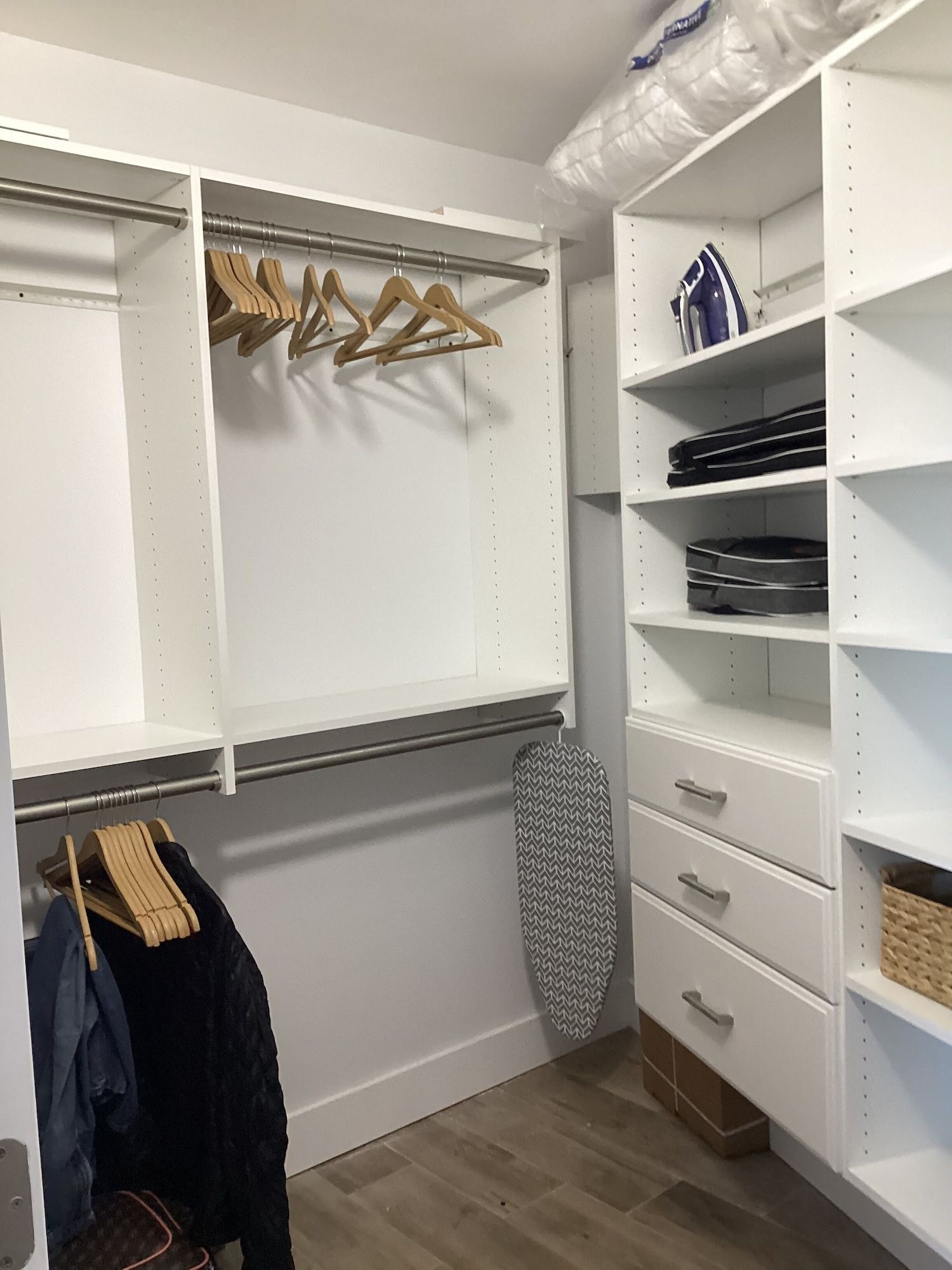 A walk in closet with lots of shelves and drawers and a ironing board.