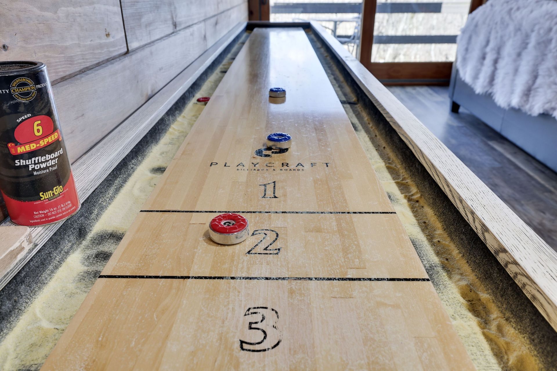 A shuffleboard game is being played on a wooden table in a bedroom.