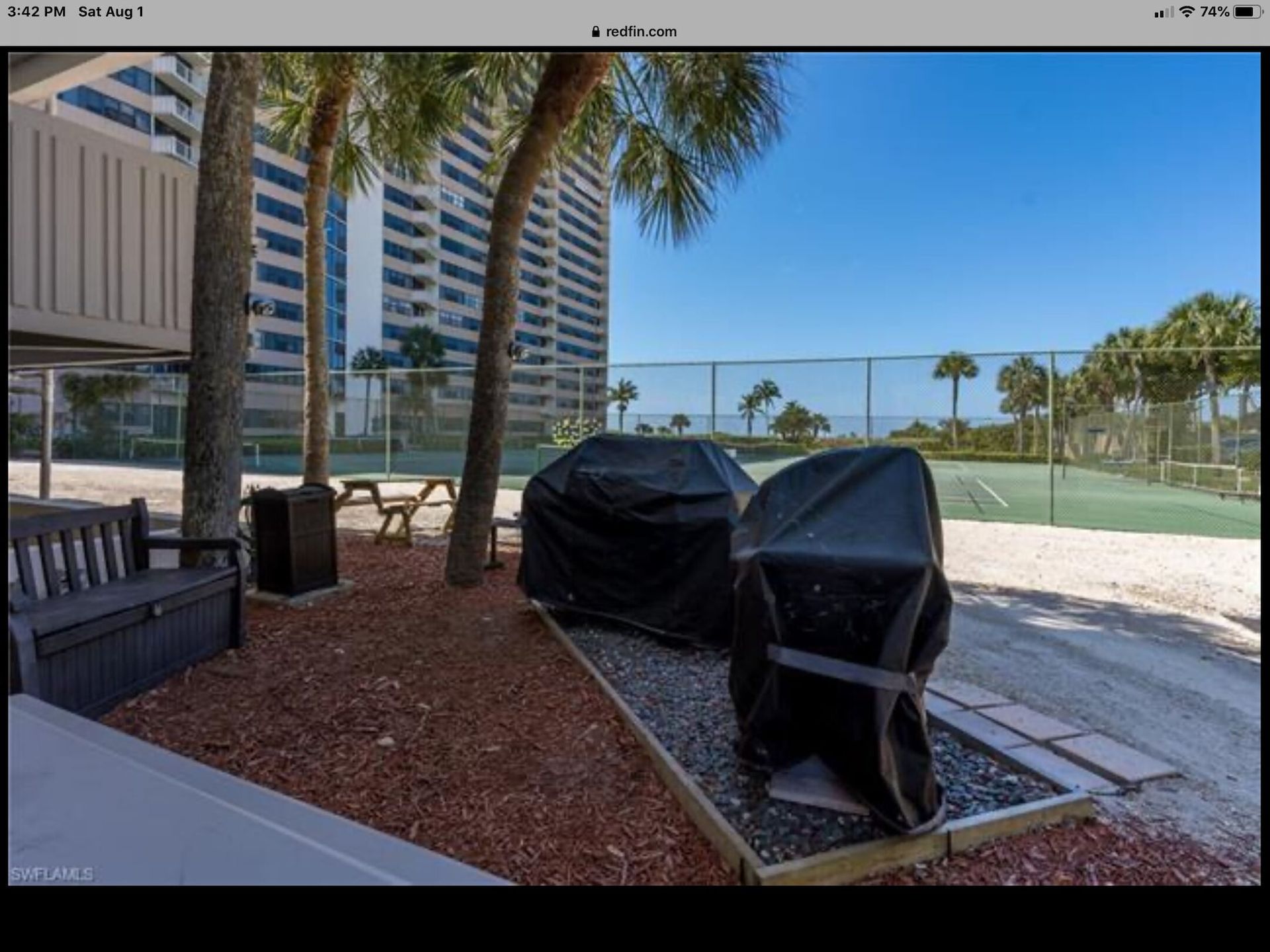 A picture of a tennis court with a bench and grills