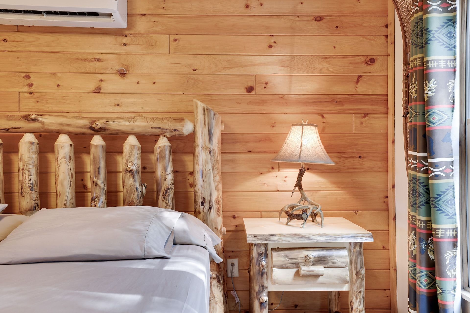 A bedroom with a bed , nightstand , lamp and air conditioner.