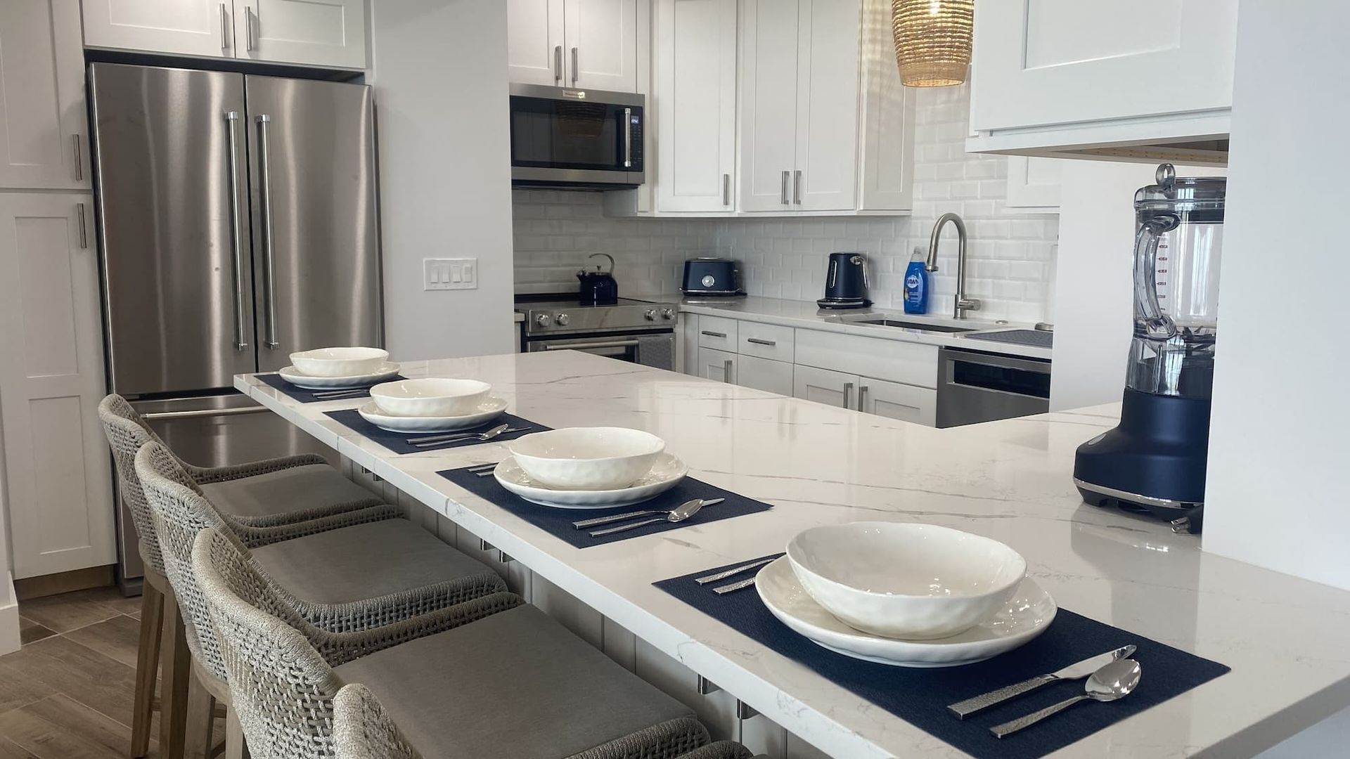 A kitchen with white cabinets , stainless steel appliances , a blender , and a long island.