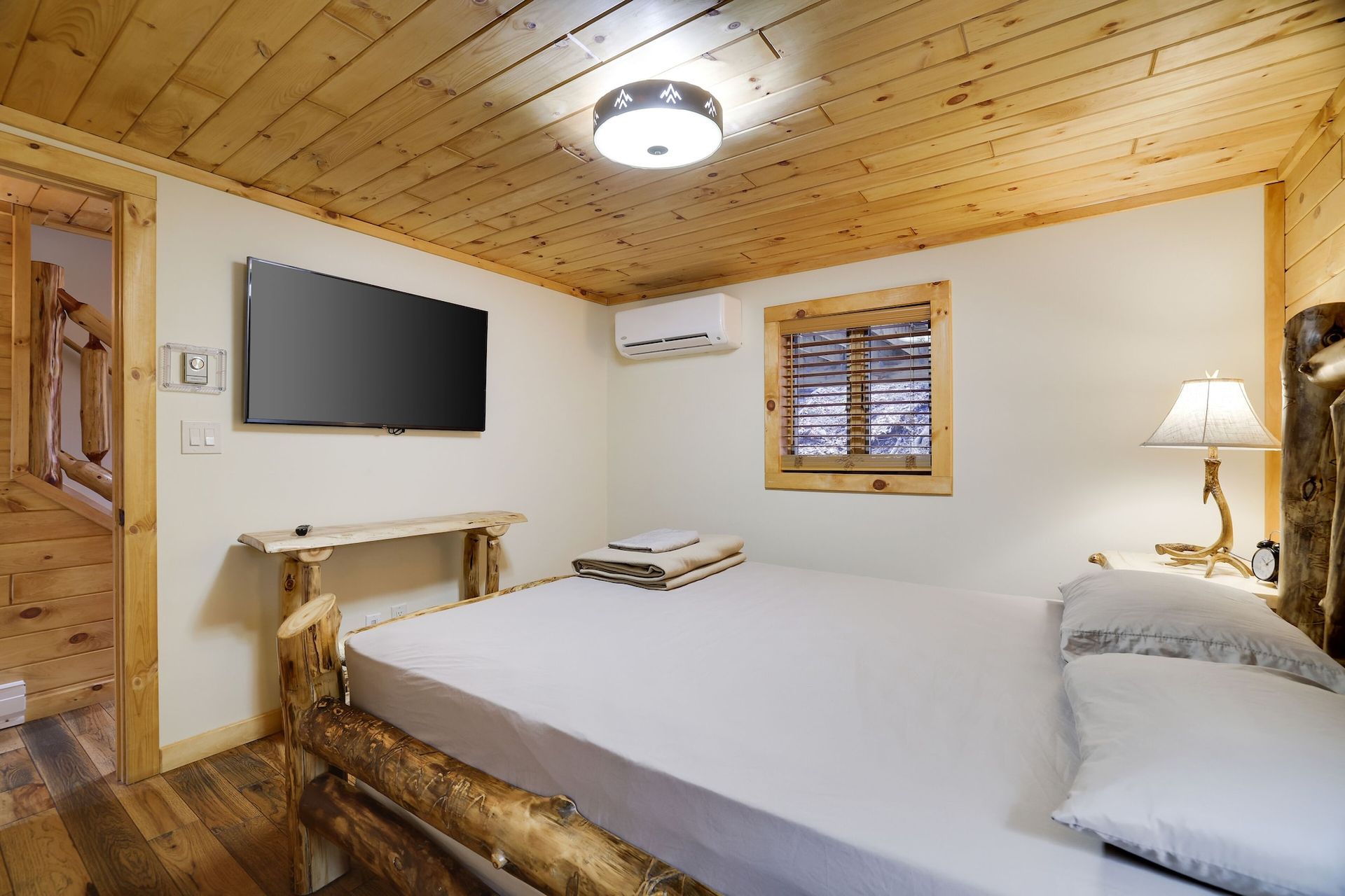 A bedroom in a cabin with a bed , television , lamp and window.