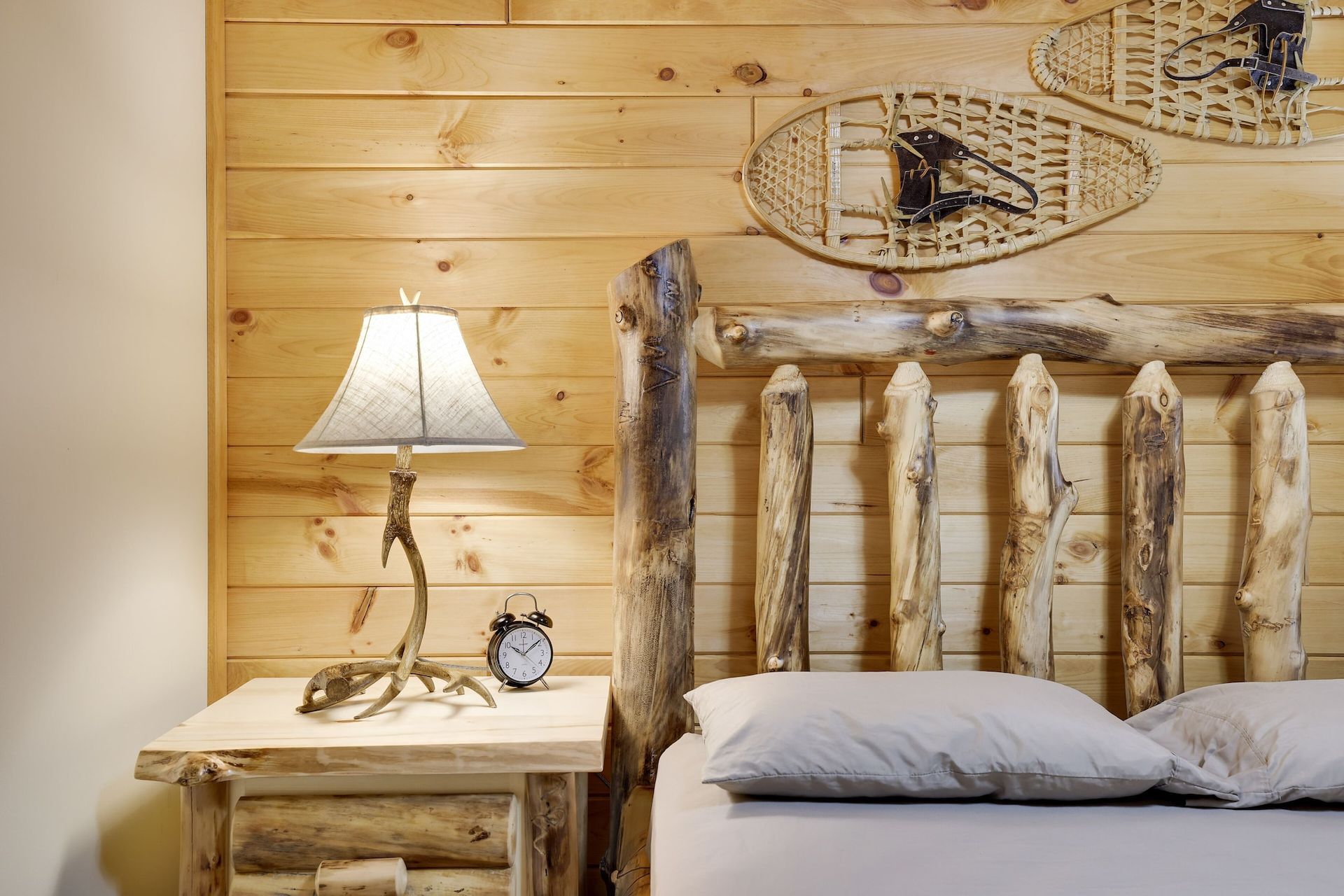 A bedroom with a bed , nightstand , lamp and snowshoes on the wall.