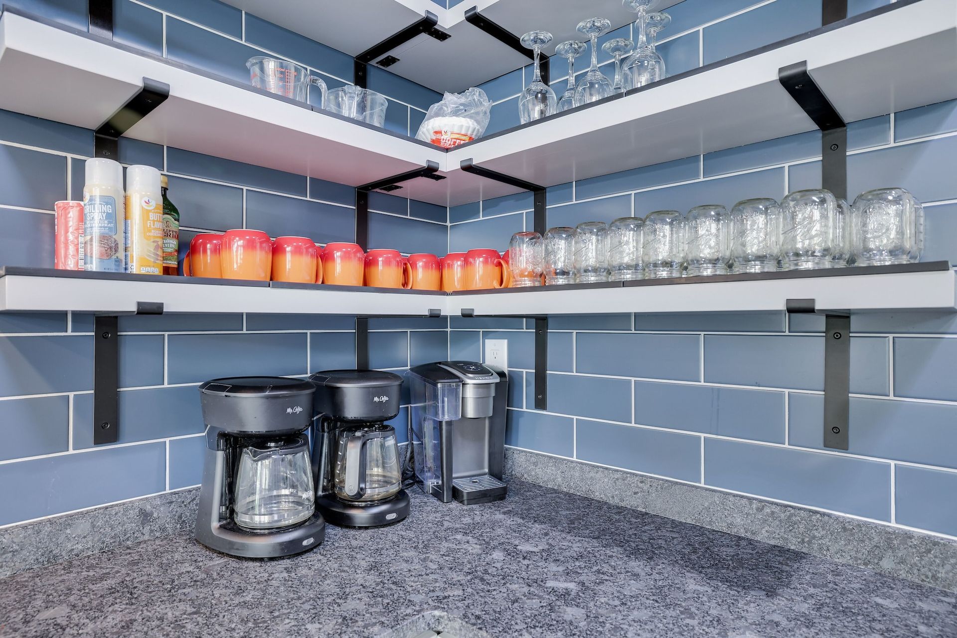 A kitchen with two coffee makers and glasses on shelves.