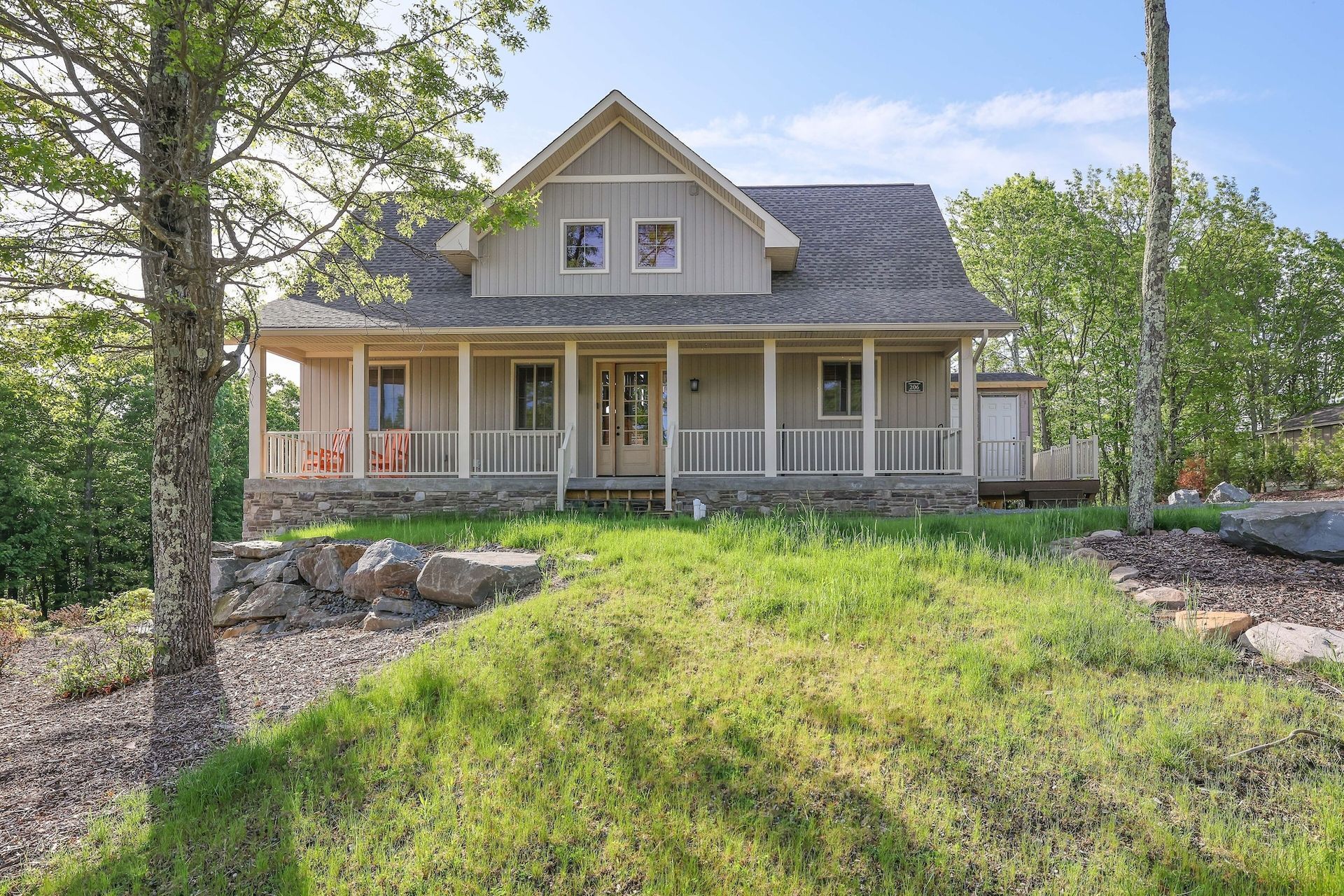 A large house with a large porch is sitting on top of a grassy hill.