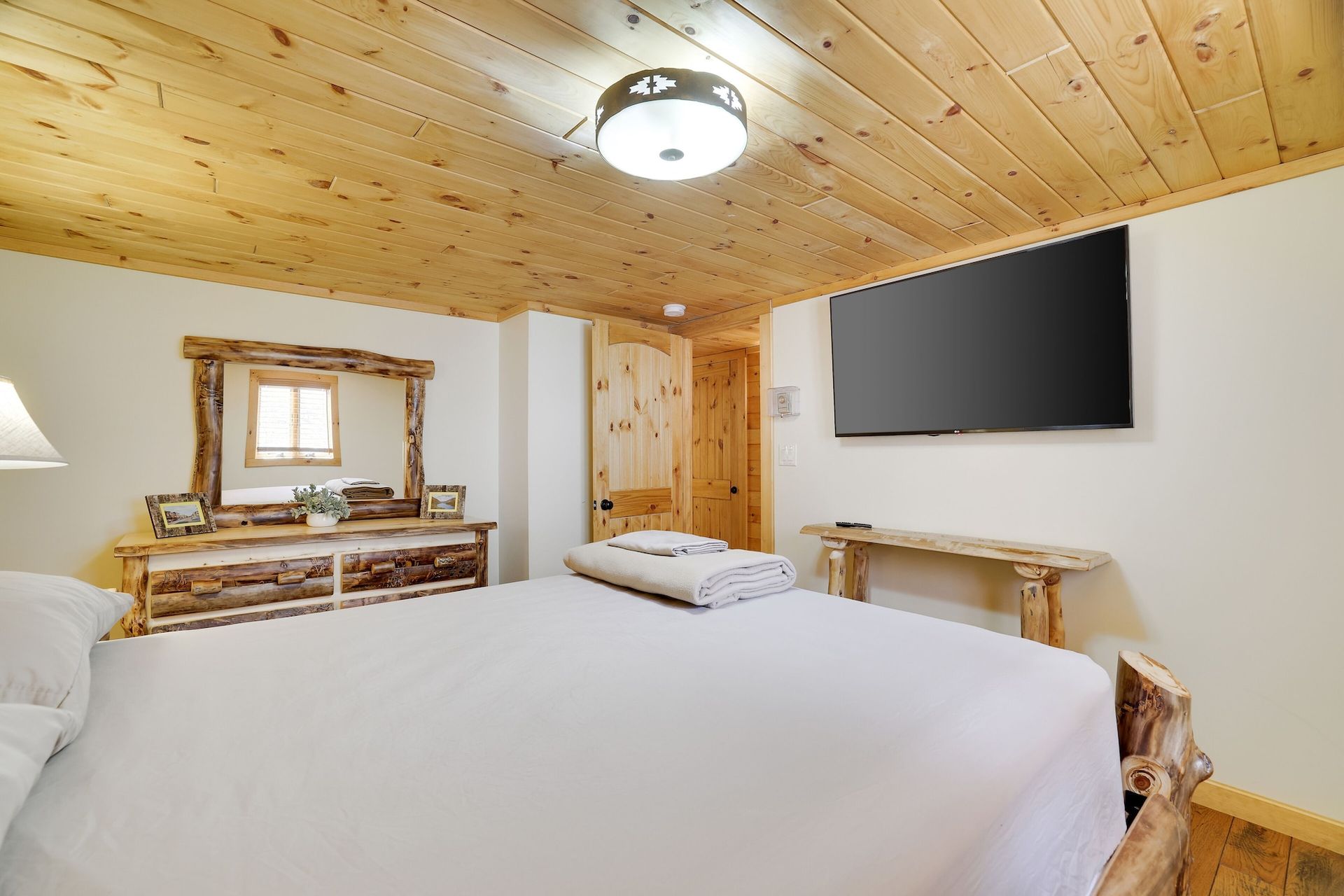 A bedroom with a king size bed , dresser , mirror and flat screen tv.