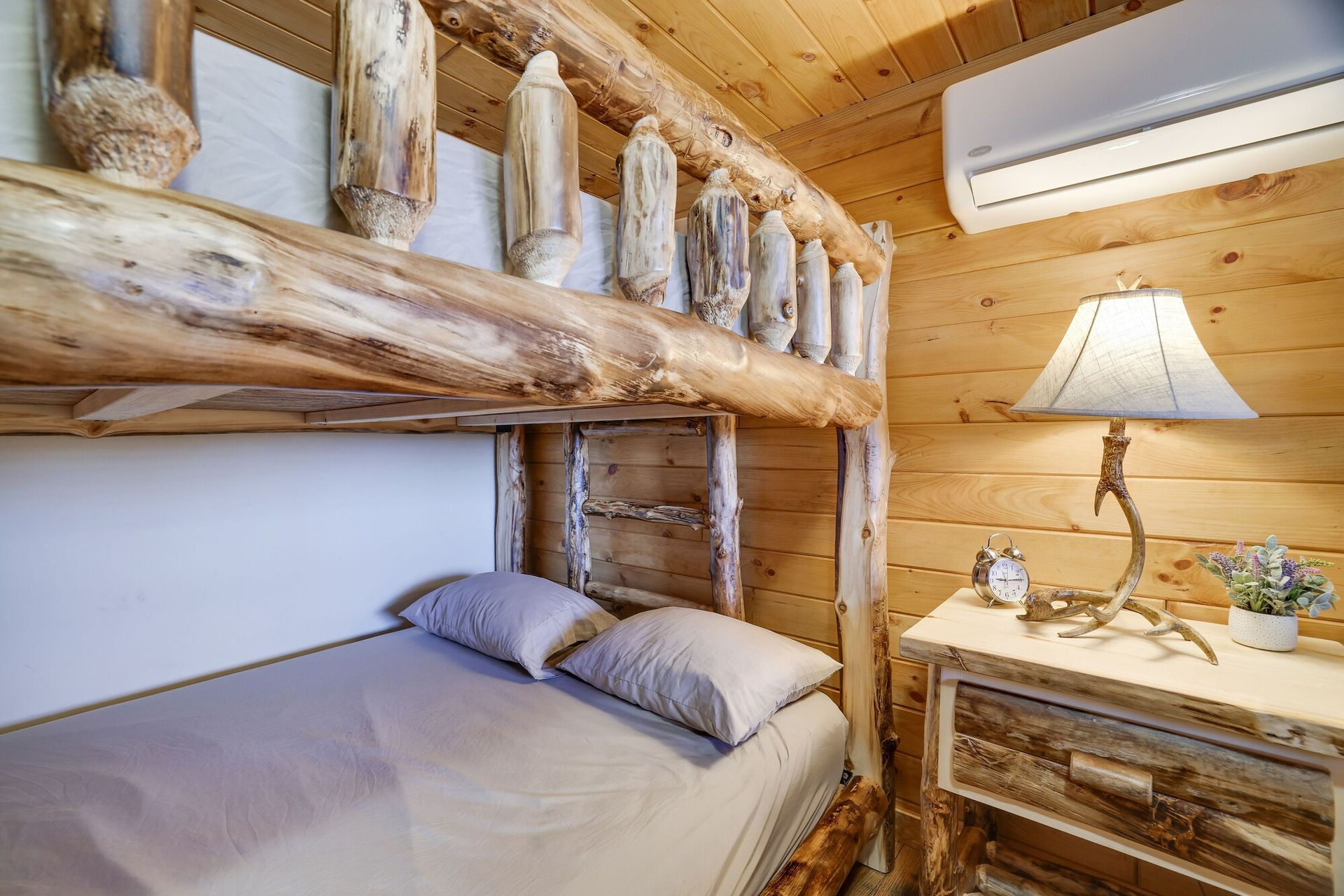 A bedroom with a bunk bed , nightstand , lamp and air conditioner.