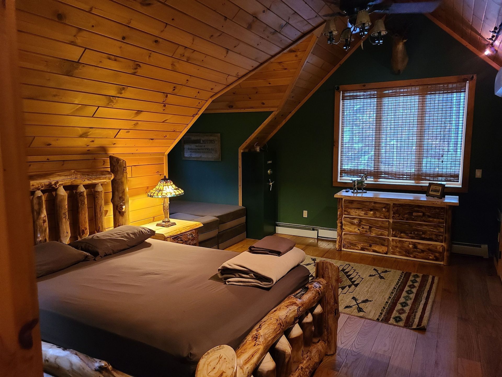 A bedroom in a log cabin with a bed , dresser , and window.