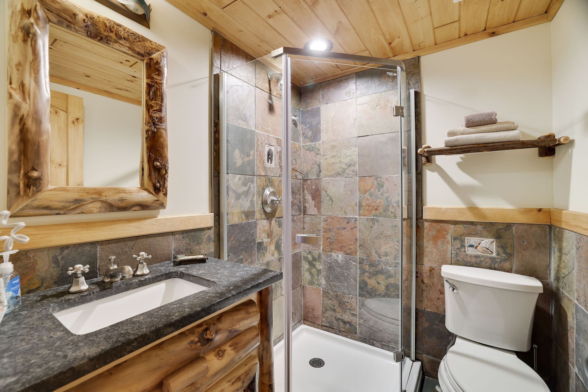 A bathroom with a toilet , sink , mirror and walk in shower.