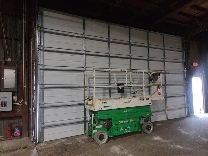 Large white industrial door with green lift in front, inside a warehouse.