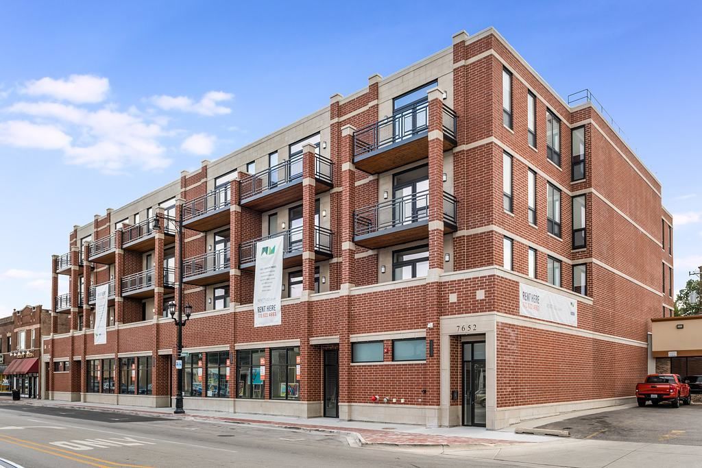 Red brick building with commercial space on the ground floor and balconies on upper floors.