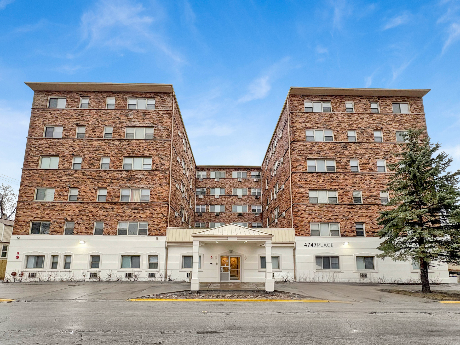 Brick apartment building with white base, glass entrance, and blue sky.