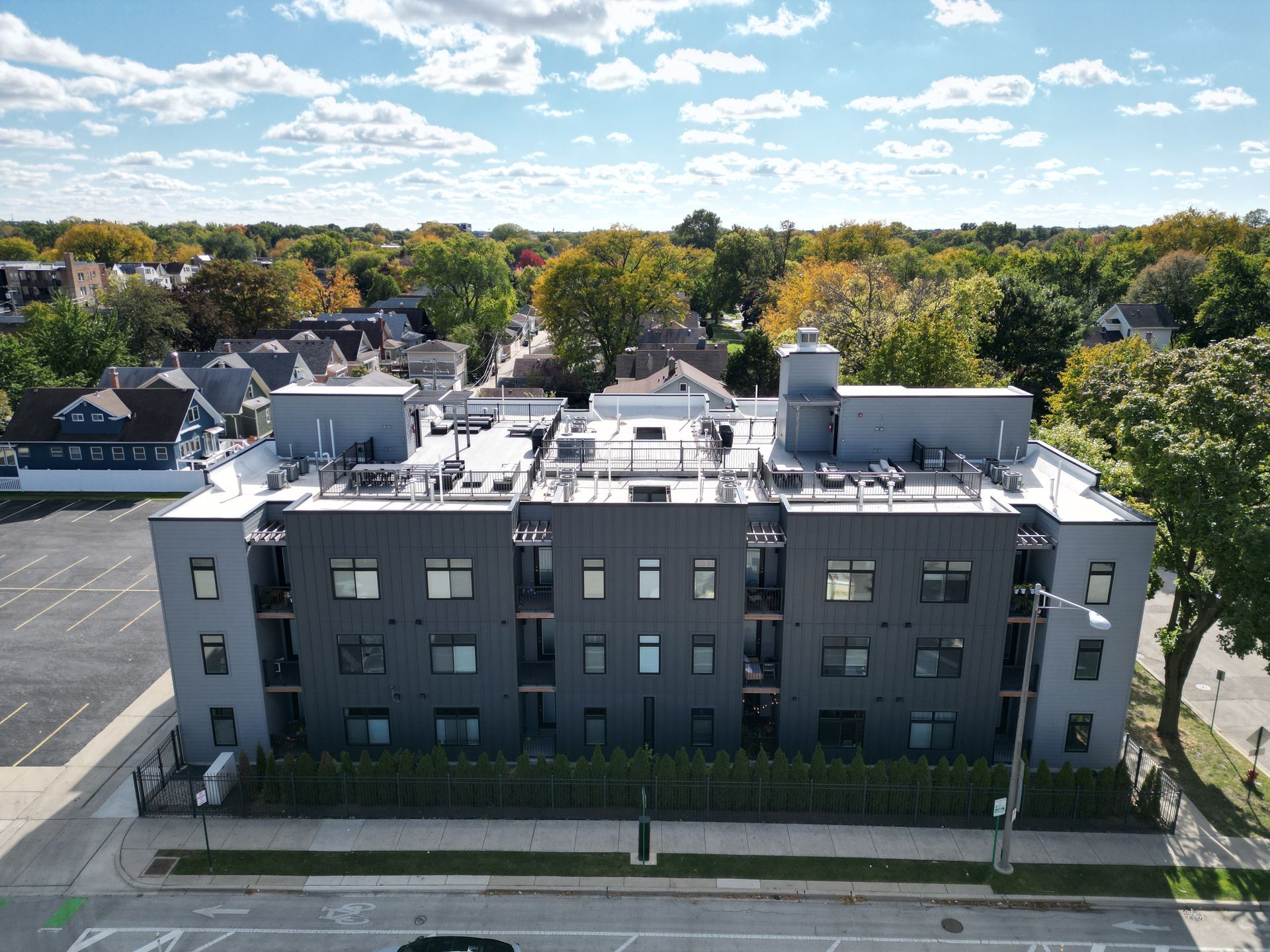Aerial view of modern multi-story apartment building with car parking; suburban setting.