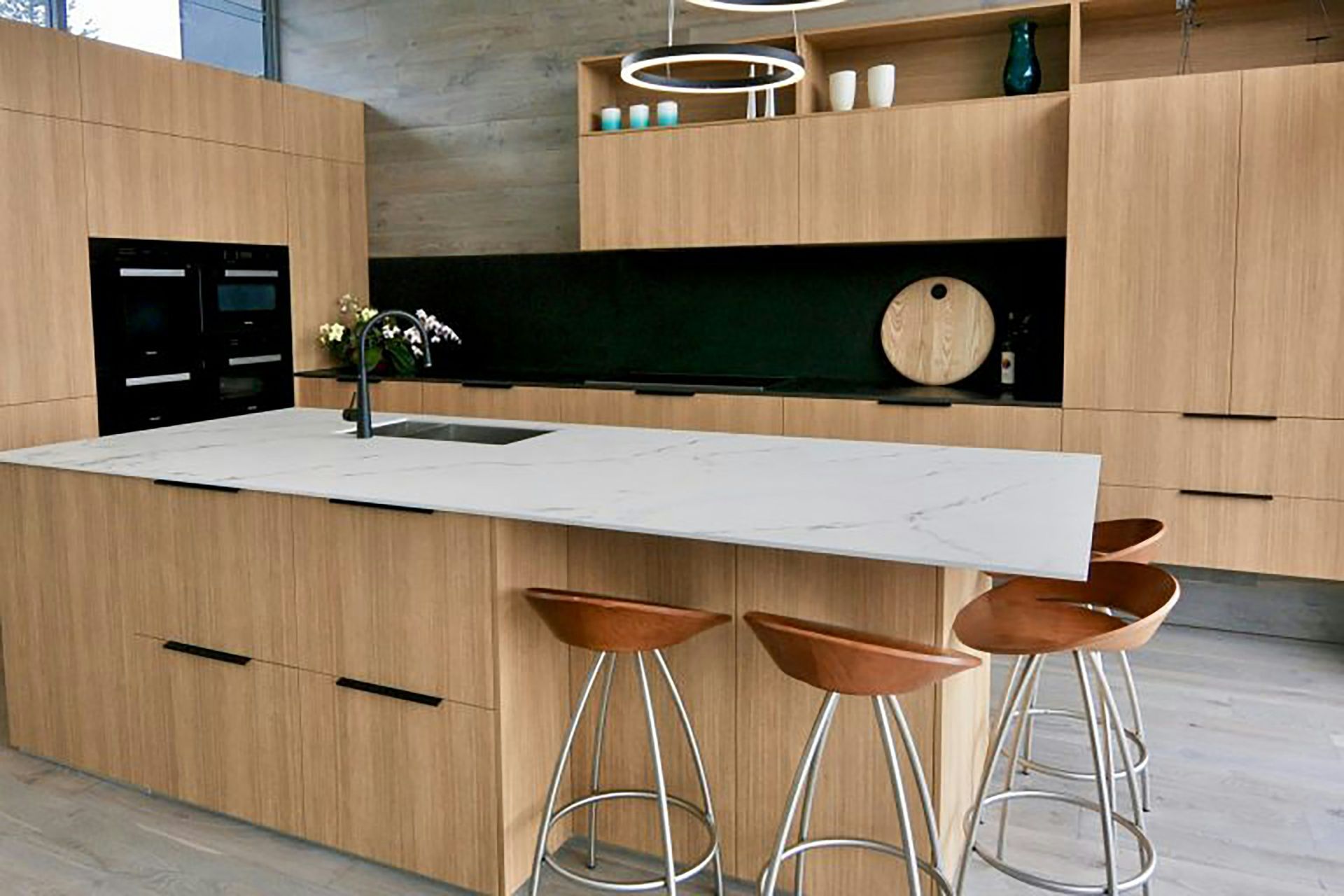 Modern kitchen with wood cabinets, white island, bar stools, and built-in appliances