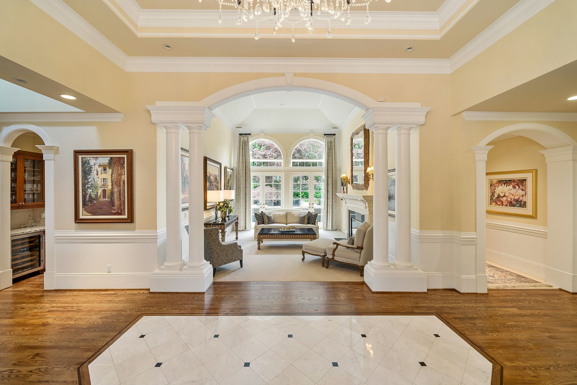 Elegant foyer with white columns, chandelier, and a view into a bright sitting room.