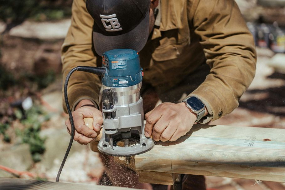 Person using a handheld power router on a wooden beam outdoors
