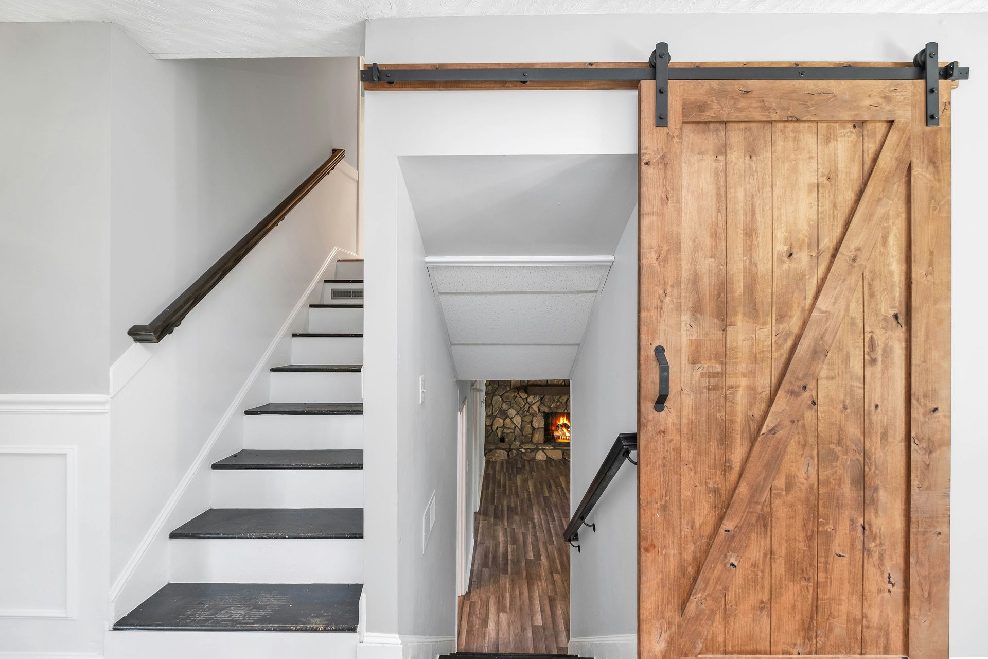 Modern staircase with black handrail and large wooden sliding barn door in a bright hallway