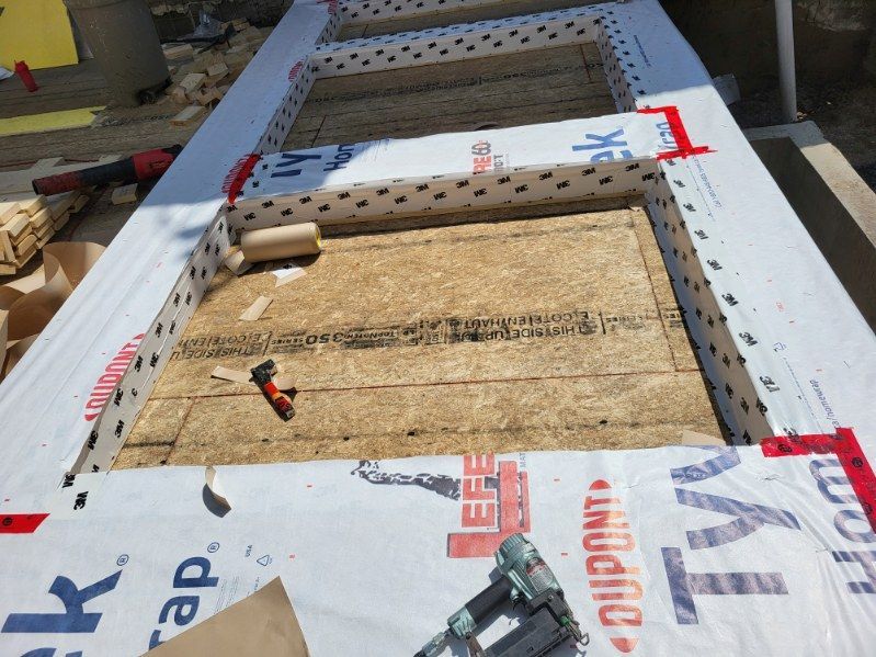 Gros plan sur la charpente d'un toit, avec son platelage en contreplaqué et son pare-vapeur Tyvek blanc, en cours d'installation sur un bâtiment.