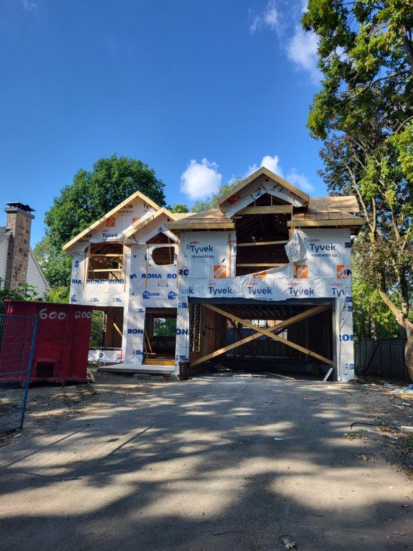 Une maison en construction avec un pare-vapeur Tyvek blanc, une ossature en bois et une benne à ordures rouge dans la cour avant.