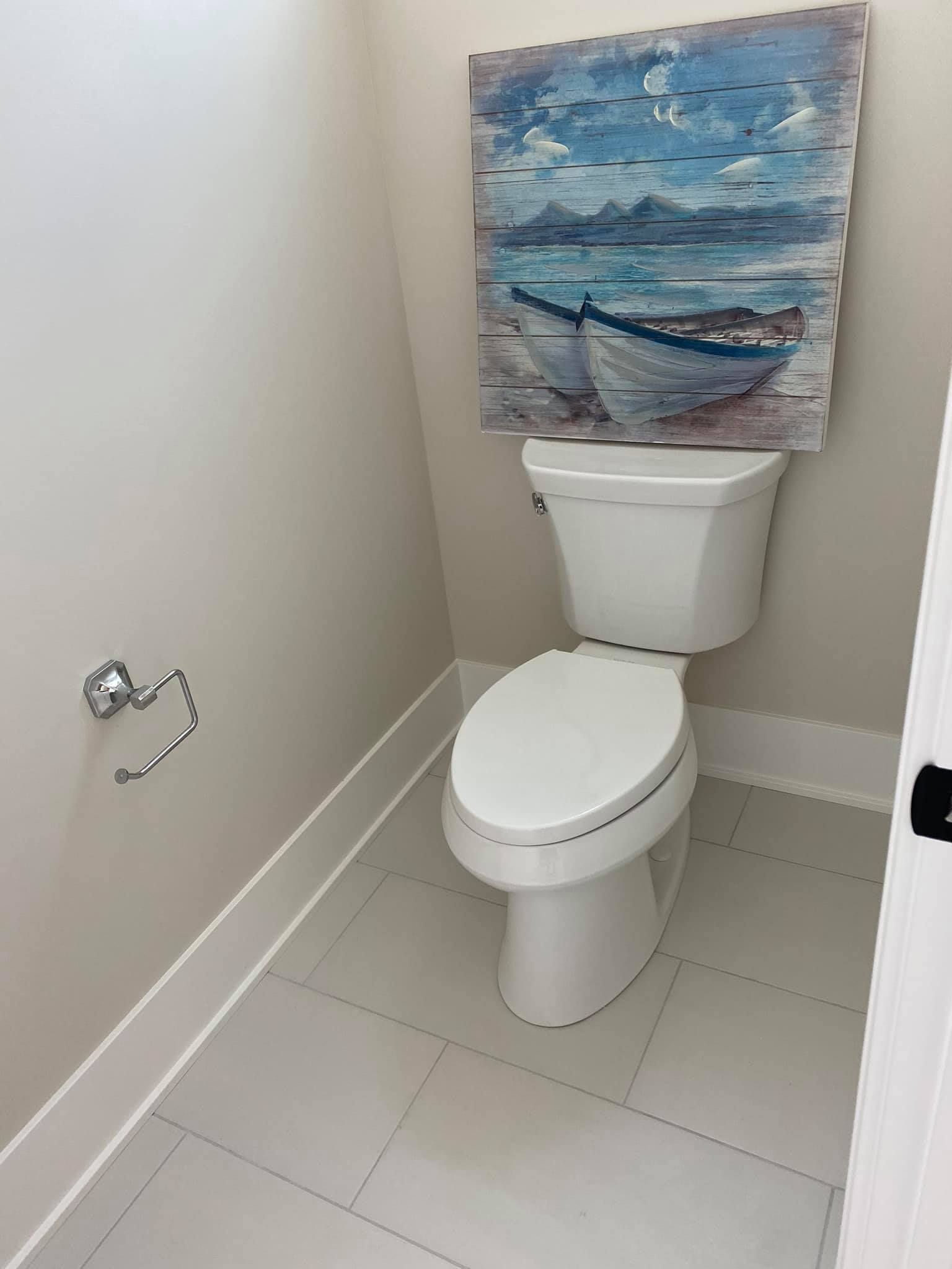 Small bathroom with a toilet below a blue ocean painting on a beige wall.