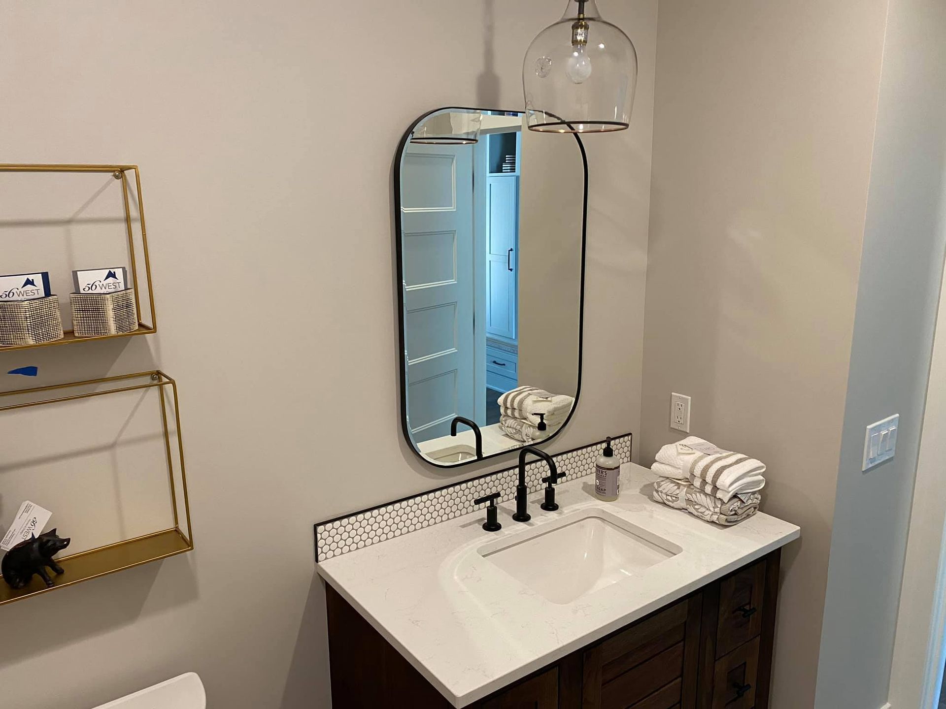 Small bathroom vanity with oval mirror, black faucet, pendant light, and folded towels on the counter.