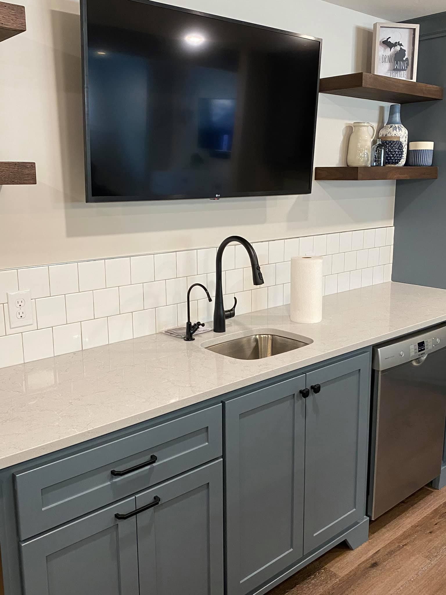 Modern kitchen with gray cabinets, black faucet, white countertop, and wall-mounted TV above the sink.