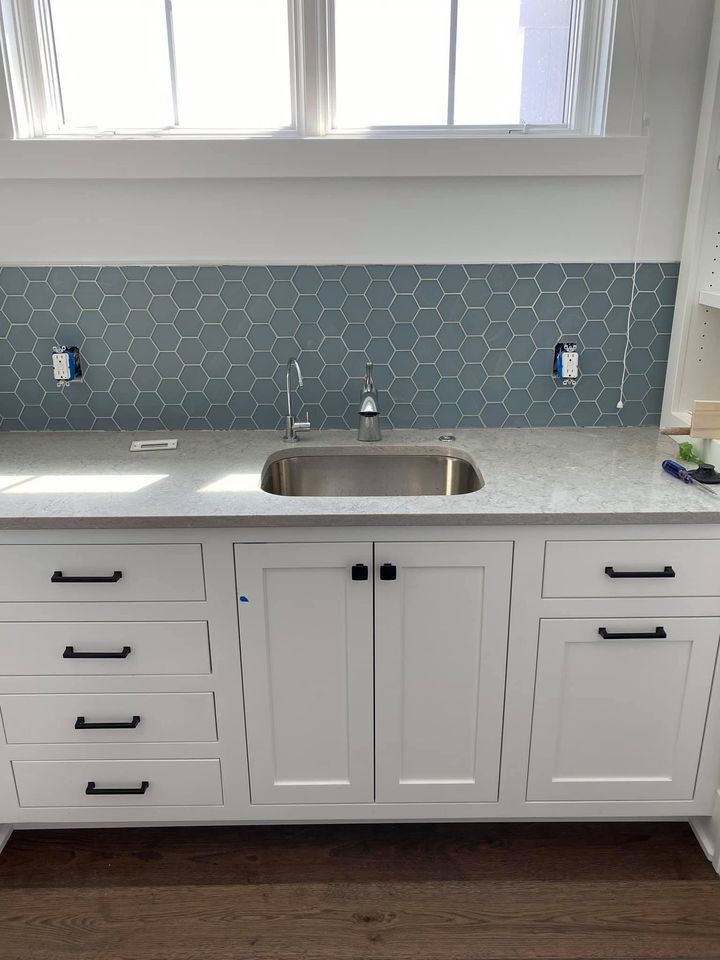 White kitchen with gray mosaic backsplash, stainless sink, and cabinets under a window