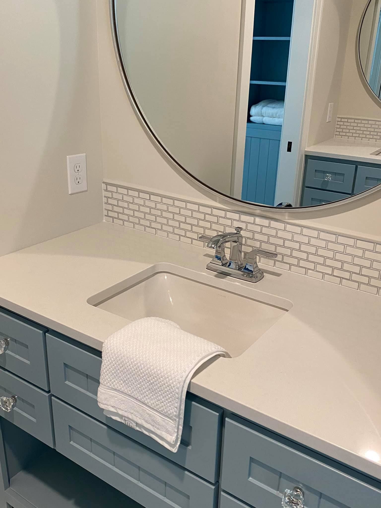 White bathroom vanity with sink, blue drawers, round mirror, and towel hanging over the counter.