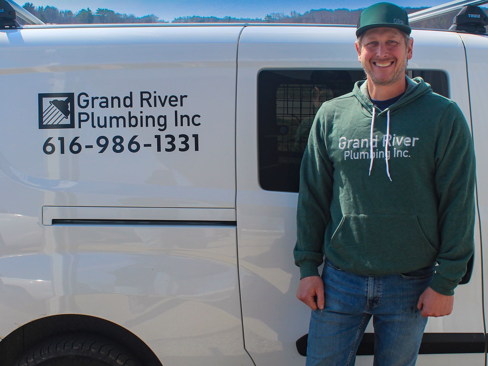 Grand River Plumbing Inc. van with smiling person in green shirt and cap standing beside it